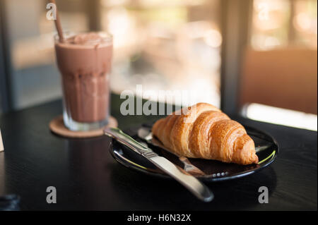 Croissant on ceramic dish with iced chocolate on wood table at cafe in afternoon time. Weekend lifestyle and activity concept. Stock Photo