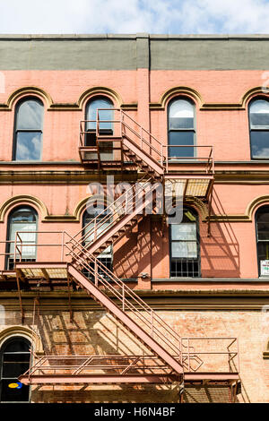 An old red rusty fire escape down a brick building Stock Photo