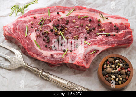 raw organic beef seasoned with peppercorns and herbs on white paper with a large sliver fork, Stock Photo