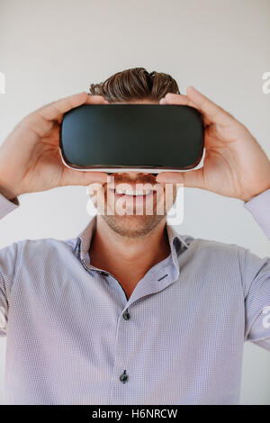 Shot of happy young man wearing virtual reality goggle against grey background. Caucasian male using VR goggle and smiling. Stock Photo