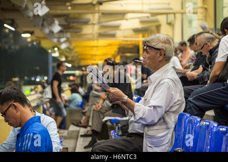 Old Chinese man smoking cigarette and reading newspaper at the Happy Valley Racecourse in Hong Kong, China. Stock Photo