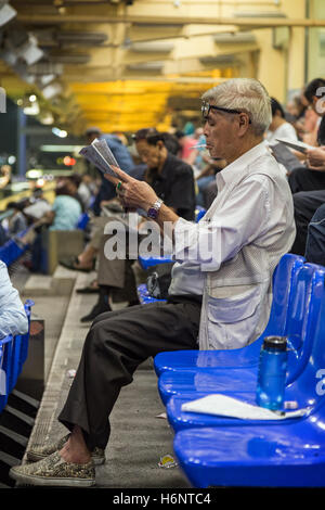 Old Chinese man smoking cigarette and reading newspaper at the Happy Valley Racecourse in Hong Kong, China. Stock Photo