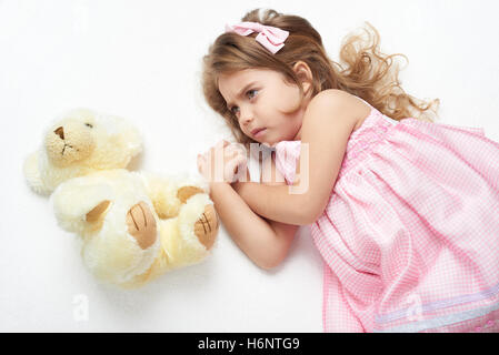 angry girl child with teddy bear lie on white towel in bed, dressed in pink Stock Photo