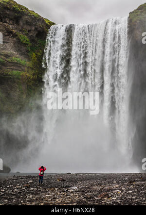 Skogafoss waterfalls falls, foss with a woman or man in Iceland, portrait format summer pt Europe falling waters Stock Photo
