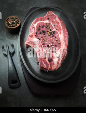 vertical dark and moody image of a raw succulent steak with a small pot of pepper corns in the background. room for copy space Stock Photo