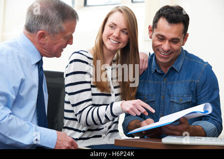 Couple With Financial Advisor Studying Document In Office Stock Photo