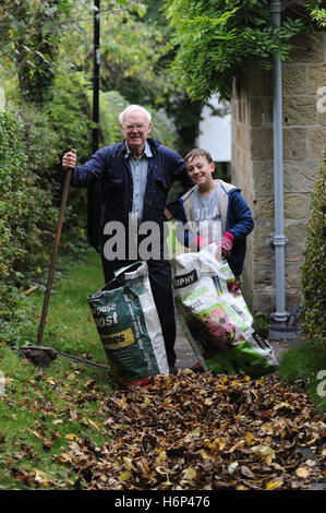 Grandfather and grandson raking autumn leaves in the garden of the family home iNorth Yorkshire , England , UK Stock Photo