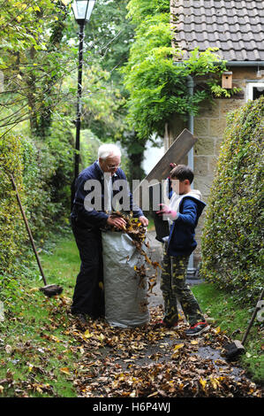 Grandfather and grandson raking autumn leaves in the garden of the family home iNorth Yorkshire , England , UK Stock Photo