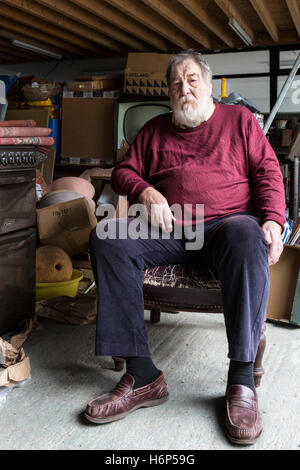 Older man sitting in an old chair in his junk shop. Cahersiveen, County Kerry, Ireland. Stock Photo