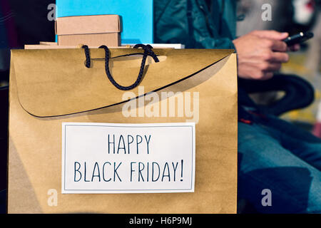 a young caucasian man sitting in a street bench using his smartphone with some gifts and a shopping bag in the foreground with t Stock Photo