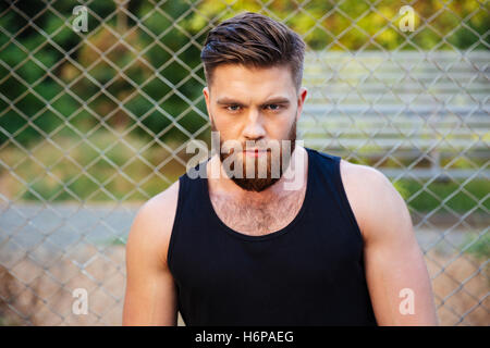 Concentrated young bearded man in tshirt looking at camera outdoors Stock Photo