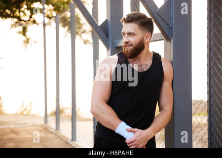 Smiling bearded young athlete standing outdoors and looking away Stock Photo