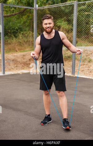 Full length portrait of a happy bearded fitness man workout with jumping rope outdoors Stock Photo