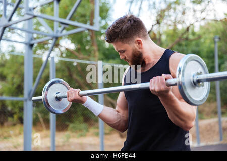 Serious young bearded fitness man lifting barbell outdoors Stock Photo