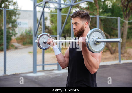 Muscular handsome bearded man workout with barbell outdoors Stock Photo