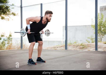 Full length portrait of a muscular fitness man doing heavy exercise using barbell outdoors Stock Photo