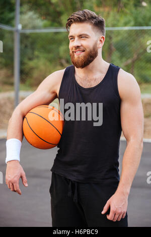 Cheerful happy basketball player standing with ball outdoors Stock Photo