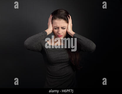 Stressed unhappy business woman closed ears the hands because not want the hear any sounds and noise on dark grey background Stock Photo