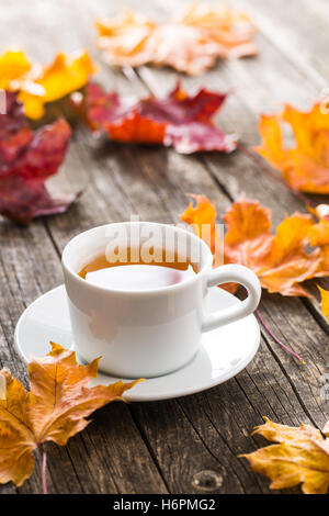 Cup of tea with autumn leaves on old wooden table. Stock Photo
