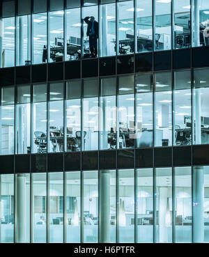 Man alone in office looking out of window at night: Coronavirus, working from home workplace stress, mental health, gig economy, loneliness...concept. Stock Photo