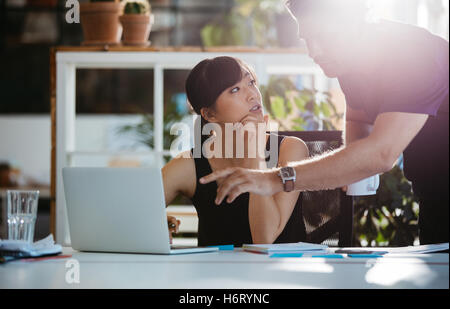 Shot of young asian woman sitting at her desk with man pointing at laptop. Two young executives working together in office