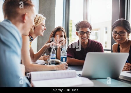 university students sitting together at table with books and laptop. Happy young people doing group study in library. Stock Photo