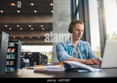 Young male student with headphones studying on the laptop. Handsome caucasian man sitting at the desk and working on laptop at p Stock Photo