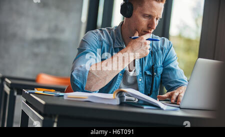 Pensive student with laptop studying in the university library. Young man using laptop and thinking. Stock Photo
