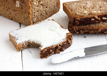 Sunflower seed loaf sliced, cream cheese spread on rustic surface. Stock Photo