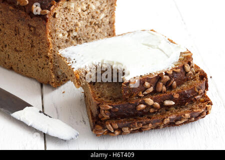 Sunflower seed loaf sliced, cream cheese spread on rustic surface. Stock Photo