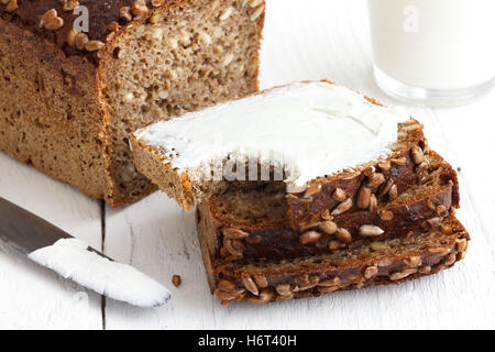 Sunflower seed loaf sliced, cream cheese spread, rustic surface, milk. Stock Photo