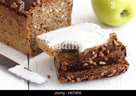 Sunflower seed loaf sliced, cream cheese spread, rustic surface, apple. Stock Photo