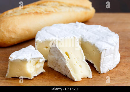White mould cheese with cut slices half eaten, and baguette, isolated on wood. Stock Photo