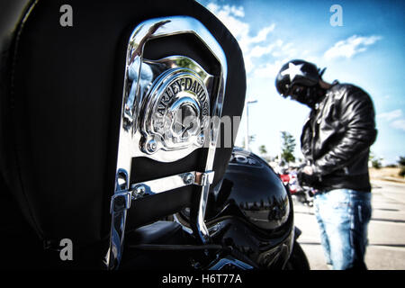 Back of Harley Davidson motorcycle with silver letters and man wearing leather jacket and helmet on the background Stock Photo
