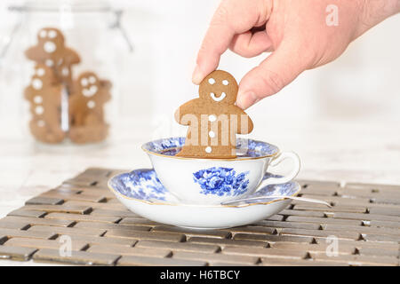 Gingerbread man being dunked into a cup of tea with jar of cookies in the background Stock Photo