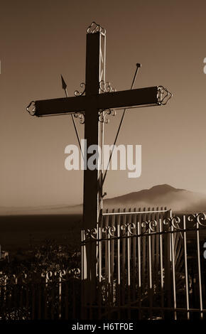 Sign of the cross Mount Vesuvius seen in the background shrouded in mist metal railings surrounding the cross protection sepia. Stock Photo