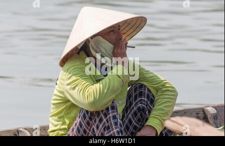 woman sitting boat smoking non la hat Hoi An, Vietnam Stock Photo