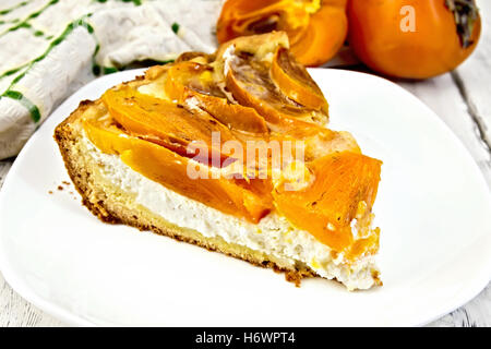 Sweet pie with curd and persimmons in a white plate, towel on a background of wooden boards Stock Photo