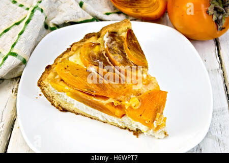 Sweet pie with curd and persimmons in a white plate, kitchen towel on a background of wooden boards Stock Photo