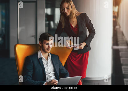 Group of business people in modern contemporary office interior, a man on yellow armchair is showing something on laptop Stock Photo