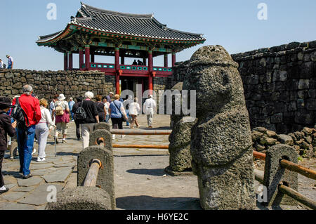 visitors walk past stone carvings at entrance gate of seongeup folk village. jeju (cheju). sth korea Stock Photo