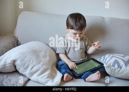 Baby boy sitting on sofa using digital tablet touchscreen Stock Photo