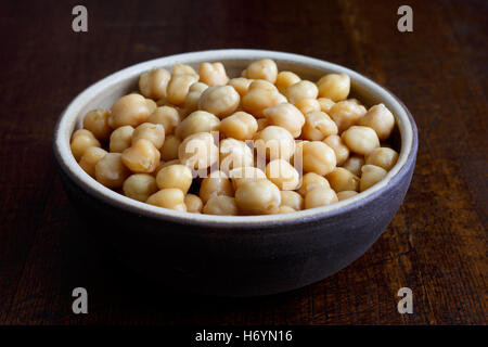 Cooked chickpeas in brown ceramic bowl isolated on dark. Stock Photo