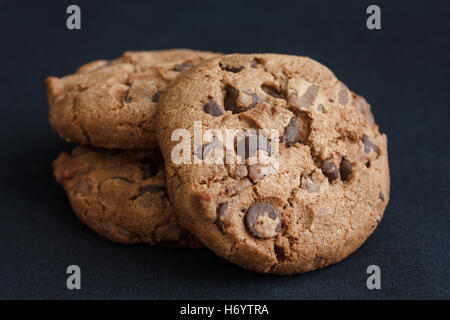 Three chocolate chip cookies on dark grey fabric. Stock Photo