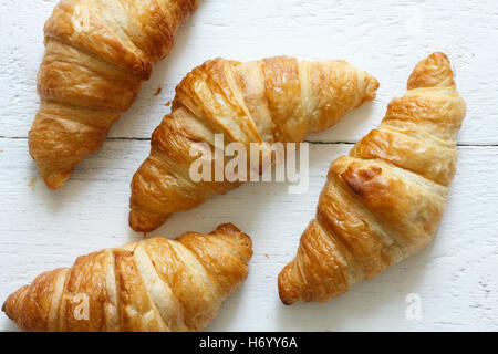 Golden croissants on rustic white wood, from above. Stock Photo