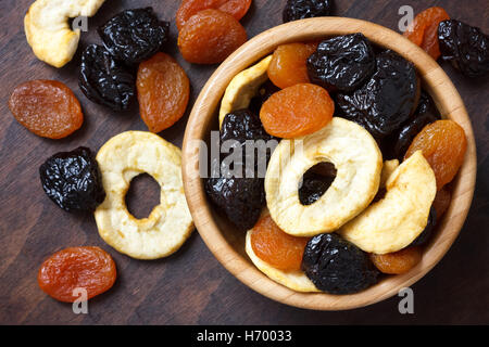 Mixed dried fruit in a wood bowl and on dark wood surface. From above. Stock Photo