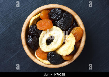 Wooden bowl of mixed dried fruit isolated on dark wood. From above. Stock Photo