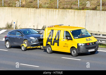 Broken down Ford car being towed along M25 motorway by yellow AA Volkswagen breakdown van with red remembrance poppy on radiator grill England UK Stock Photo