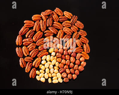 Assorted nuts (Pecan, Hazelnuts and Roasted Salted Peanuts) in a circle form on a black background Stock Photo