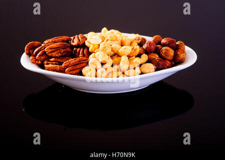 Assorted nuts (Pecan, Hazelnuts and Roasted Salted Peanuts) in a white plate on a black background Stock Photo